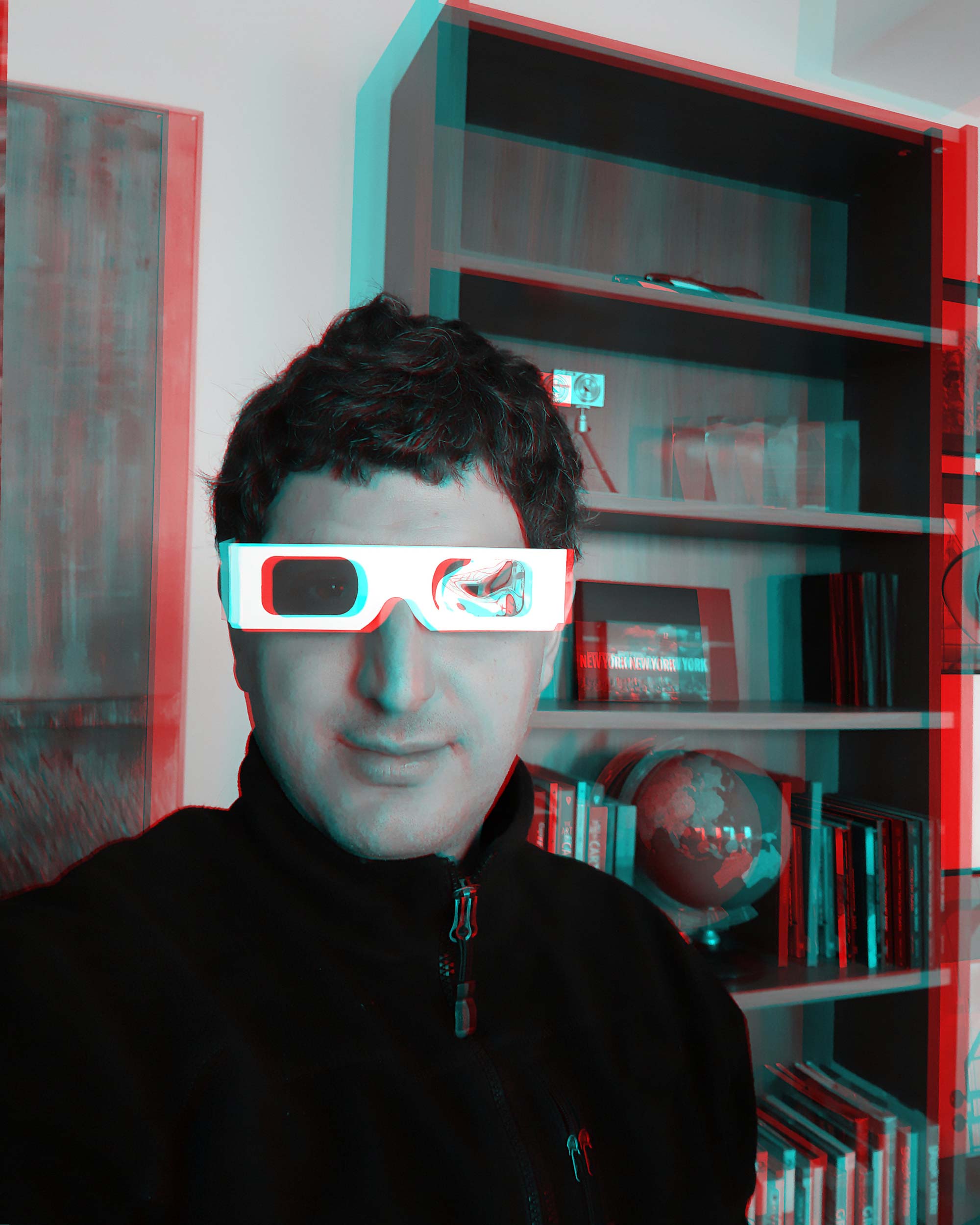 Spiros Staridas wearing 3D glasses in a creative workspace with books and a globe, representing the artistic and scientific spirit of Staridas Geography.